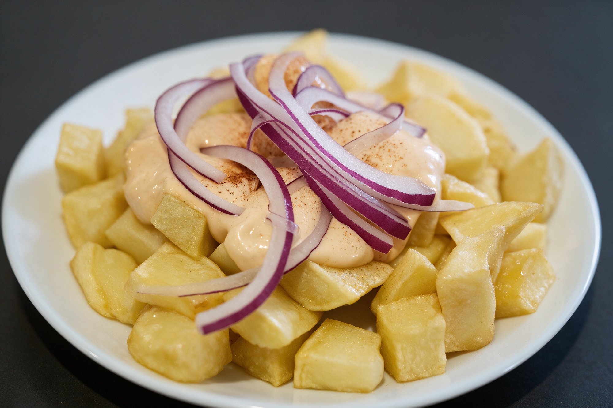 Patatas con Salsa de Tapería Alba, patatas fritas con salsa cremosa y cebolleta en plato blanco, vista desde arriba